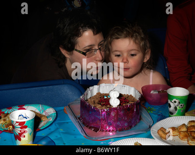 Madre e figlia di tre anni soffiando le candeline sulla torta di compleanno Foto Stock