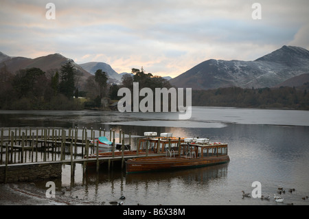 Viaggio turistico barche ormeggiate a Keswick marina in una giornata invernale a derwentwater in inglese con montagne innevate sullo sfondo Foto Stock