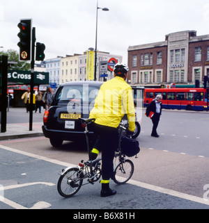 Un taxi & imprenditore ciclista indossa un casco in sella ad una bicicletta Brompton bicicletta pedalando a lavorare vicino a Kings Cross Station Londra Inghilterra KATHY DEWITT Foto Stock