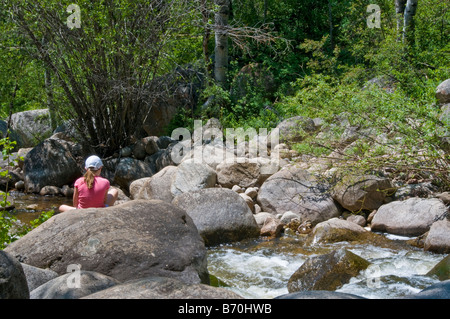 In estate, il ruggito di elevata di spruzzi di acqua su grossi massi lungo Aspen cacciatore della Creek Trail attrae una giovane donna escursionista. Foto Stock