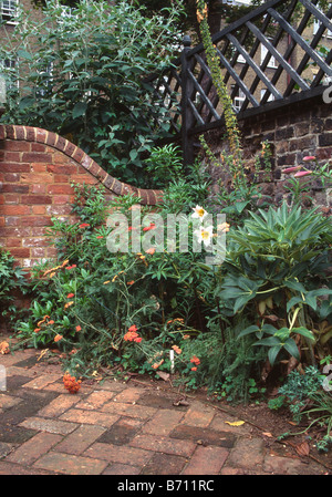 Estate piante fiorite in frontiera pavimentato in città giardino con curve di parete di mattoni e i pergolati in legno sulla parete Foto Stock