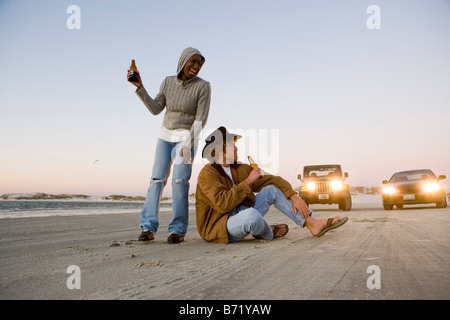 Giovani interracial giovane azienda bottiglia di birra sulla spiaggia di fronte delle vetture Foto Stock
