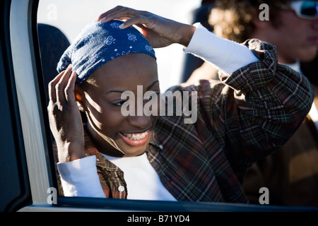 Giovane americano africano donna che indossa bandana cercando in vista laterale specchio della vettura Foto Stock