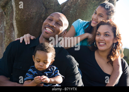 Felice famiglia americana africana seduta mediante una struttura ad albero in cortile Foto Stock