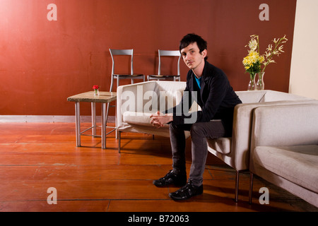 Elegante giovane uomo seduto in soggiorno moderno Foto Stock