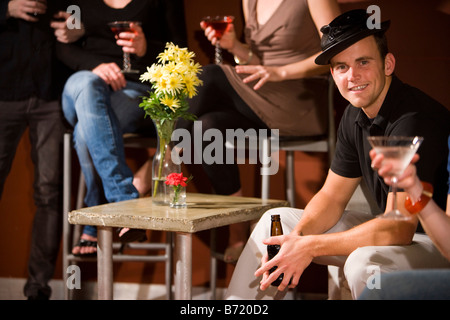 Ritratto di giovane sorridente uomo seduto e avente un drink con gli amici Foto Stock