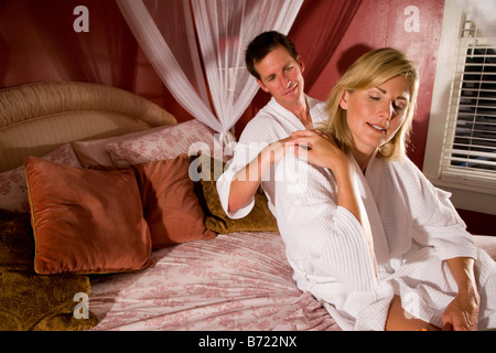 Man mano appoggiata su alle spalle della donna mentre è seduto nel letto Foto Stock