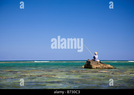 L'uomo la pesca utilizzando la casa con asta di pesca mentre è seduto su una roccia nell'Oceano Indiano al largo della costa di Mauritius Foto Stock