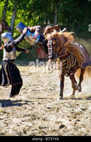Immagine di due uomini vestiti in stile medievale abbigliamento e armor uno in sella ad un cavallo e salta su un altro uomo in una giostra tou Foto Stock