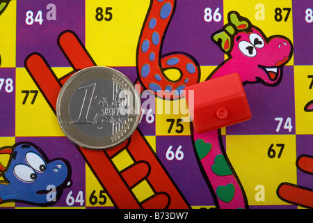 Un Euro monete e toy red house su un serpenti e scale board con euro sulla scala e la casa del serpente Foto Stock