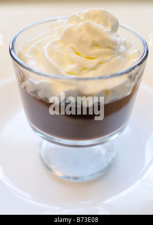 Budino di cioccolato la torta con panna montata in un vetro ciotola da dessert su sfondo bianco. Foto Stock