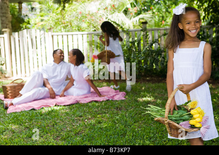 Afro-americano di ragazza con cesto fiorito, picnic in famiglia in background Foto Stock