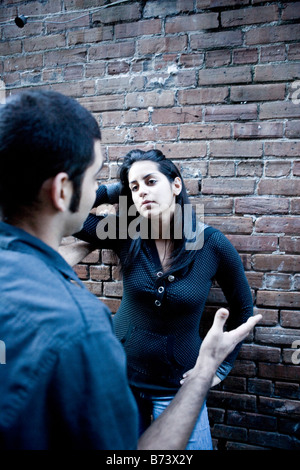 I giovani ispanici giovane parlando fuori appoggiato contro un muro di mattoni Foto Stock