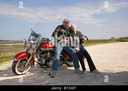Felice senior biker giovane seduto appoggiato contro la motocicletta su strada sterrata Foto Stock