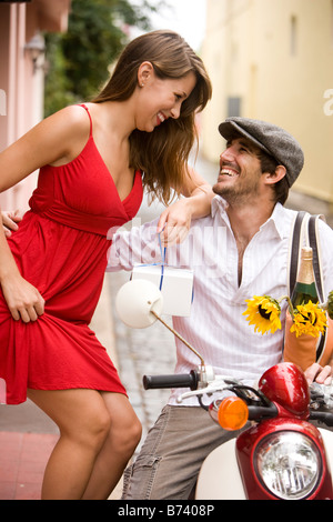 Piuttosto giovane donna sul marciapiede parlando di uomo bello su scooter Foto Stock