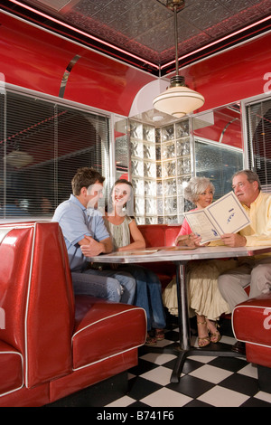 Coppia giovane con i genitori seduto in cabina di un vecchio stile diner parlando Foto Stock