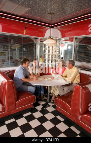 Coppia giovane con i genitori seduto in cabina di un vecchio stile diner parlando Foto Stock