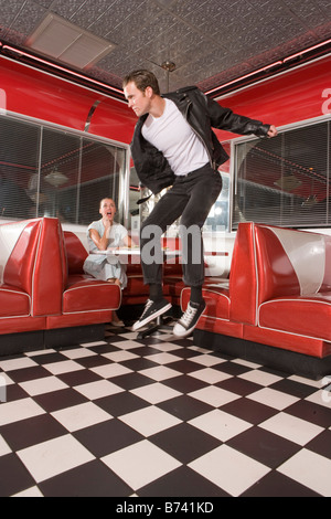 Giovane uomo jumping in midair negli anni cinquanta a style diner, fidanzata a guardare Foto Stock