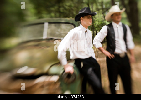 Due giovani uomini che indossano cappelli da cowboy e western convenzionale appoggiata sul vecchio carrello Foto Stock