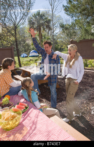 Giovani famiglie felici giocando al tavolo da picnic vicino al campeggio Foto Stock