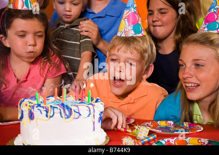 Ragazzo che un desiderio e soffiare fuori candele alla festa di compleanno Foto Stock