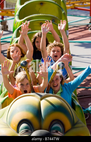 I bambini a cavallo di un roller coaster in un parco di divertimenti Foto Stock