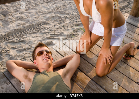 Giovane uomo disteso sul ponte di legno a beach, donna inginocchiato accanto a Foto Stock