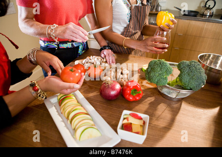 La sezione centrale di tre multi-etnico donne preparare insalata in cucina Foto Stock