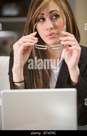 Piuttosto giovane donna che lavorano su laptop, pensando che con gli occhiali in mani Foto Stock