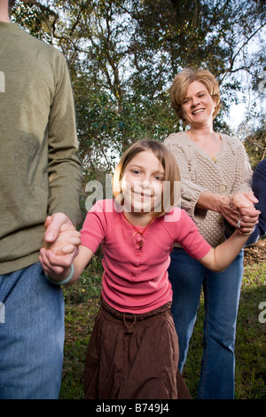 Ragazza camminare all'aperto tenendo le mani dei genitori Foto Stock