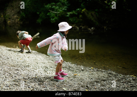 Bambini scagliare pietre nel flusso bambina di cinque anni e sei anni di fratello Foto Stock