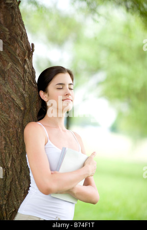 Giovane donna appoggiata sul tronco di albero Foto Stock