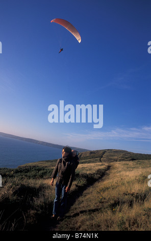 Donna e bambino nello zaino camminando sul sentiero costiero vicino Newgale con parapenter Pembrokeshire Wales UK Europa Foto Stock