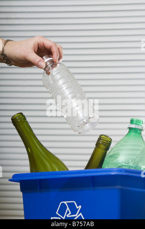 Casalinga aggiunta alla casella blu pieno di bottiglie per il riciclaggio Foto Stock