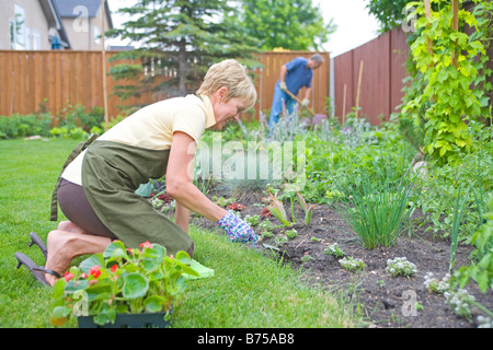 Senior donna lavora in giardino nel cortile con il marito in background, Winnipeg, Manitoba, Canada Foto Stock