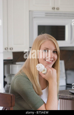 Giovane donna azienda compatta lampadina fluorescente in cucina, Brandon, Manitoba, Canada Foto Stock