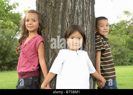 Cinque e sette anni ragazze e sette anni di vecchio ragazzo tenere mani attorno ad albero, Winnipeg, Canada Foto Stock