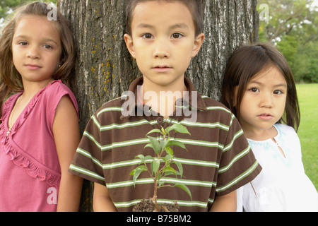 Cinque e sette anni ragazze e sette anni di old boy holding piccolo albero, Winnipeg, Manitoba, Canada Foto Stock