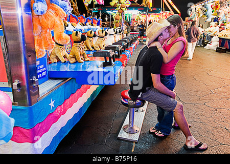 Coppia adolescenti baciare reciprocamente in un parco di divertimenti Foto Stock