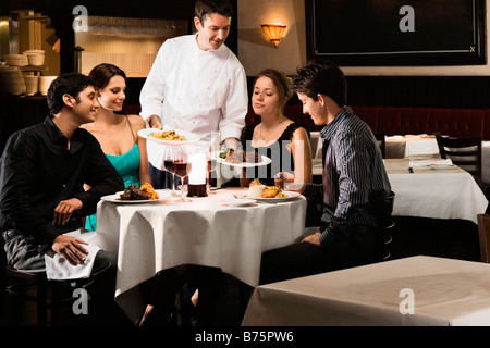 Lo chef maschio che serve cibo a due coppie giovani seduti in un ristorante Foto Stock
