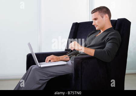 Profilo laterale di un giovane uomo seduto in poltrona e al lavoro su un notebook Foto Stock