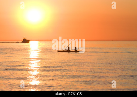 Il Tandem dei rematori in kayak sul lago Michigan al tramonto con powerboat in background Foto Stock