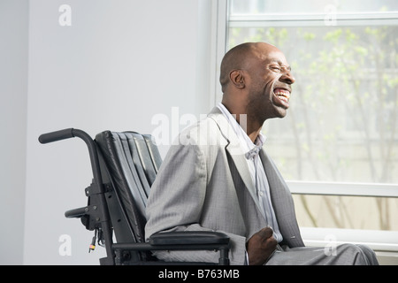 Imprenditore con paralisi cerebrale seduto in una sedia a rotelle e sorridente Foto Stock
