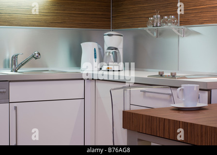 Bianco moderno interior design cucina angolo con apparecchi elettrici, tavolo, sedia, mug, un lavandino e un armadio. Foto Stock