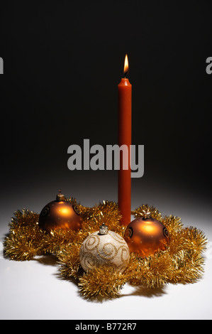 Oro decorazione di Natale tema tre baubles e una candela Foto Stock