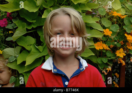 Bella giovane ragazzo con un sorriso raggiante che pongono in giardino con il suo fratello più giovane nascosto in al suo fianco. Foto Stock