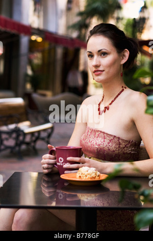 Giovane donna seduta in un outdoor cafe tavolo a bere un cappuccino Foto Stock