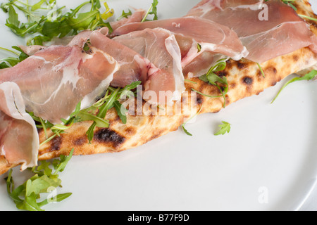 Calzone con spek e rucola. La pizza italiana con prosciutto affumicato. La messa a fuoco del prosciutto. Foto Stock