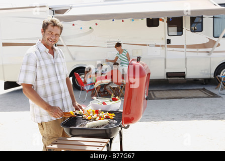 L uomo alla brace famiglia e motor home background Foto Stock