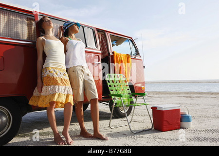 Giovani donne appoggiata contro van sulla spiaggia Foto Stock